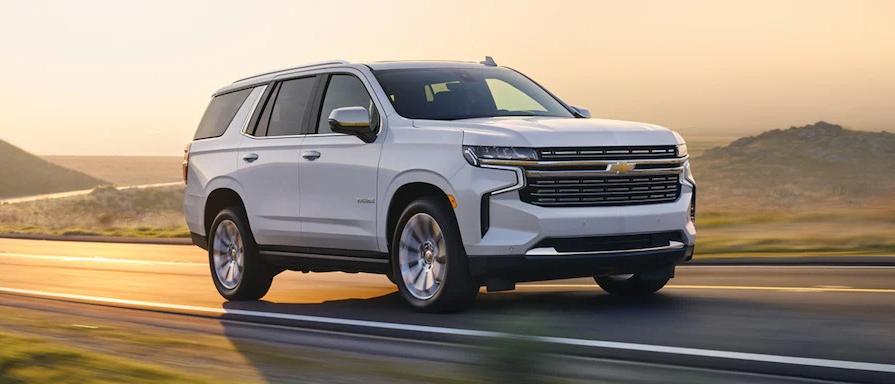 A silver 2023 Chevrolet Tahoe driving down a road with a scenic mountain background